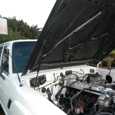 Installed FJ Cruiser Hood Strut holding up the open hood of a white vehicle to showcase the engine bay.