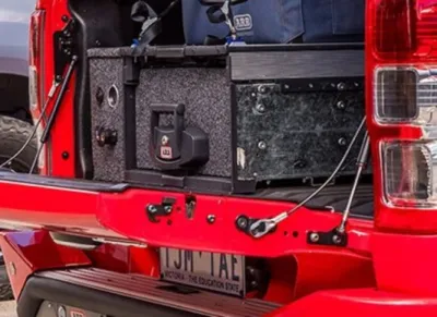 Red truck with an open tailgate showing a ford f150 tailgate assist and ARB cargo drawers.