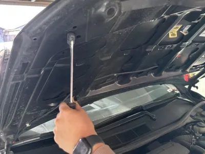 Person using a screwdriver to remove a Toyota Camry hood strut.